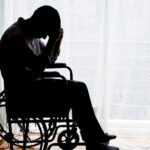 Man in wheelchair in dark silhouette holding head in hands_s