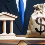 A money bag on a scale with a small wooden courthouse façade_s