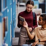 young man in a wheel chair looking at a book with a young woman_s