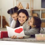 Mother with two young daughters opening a Mother’s Day card_s