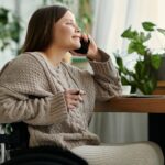 young woman sits in wheelchair, smiling as she talks on her phone