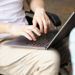 Man in wheelchair works on laptop on street next to woman_s