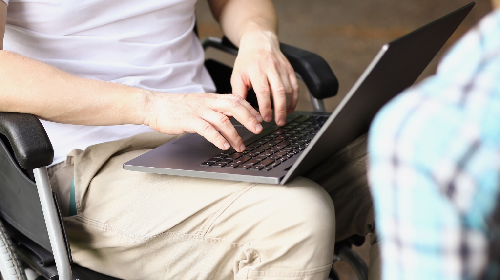 Man in wheelchair works on laptop on street next to woman