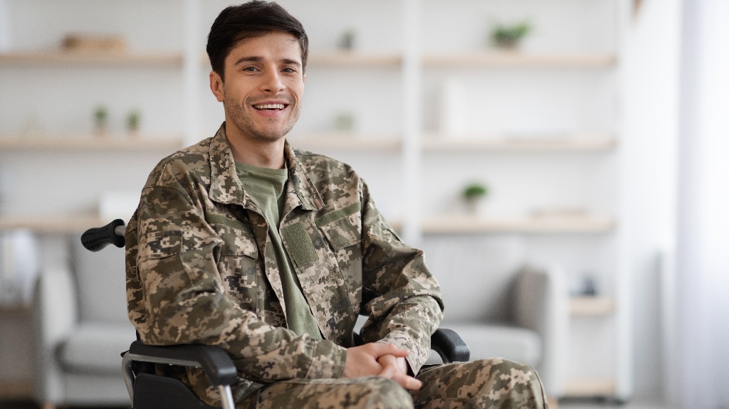 Happy positive young man in camouflage uniform sitting in wheelchair