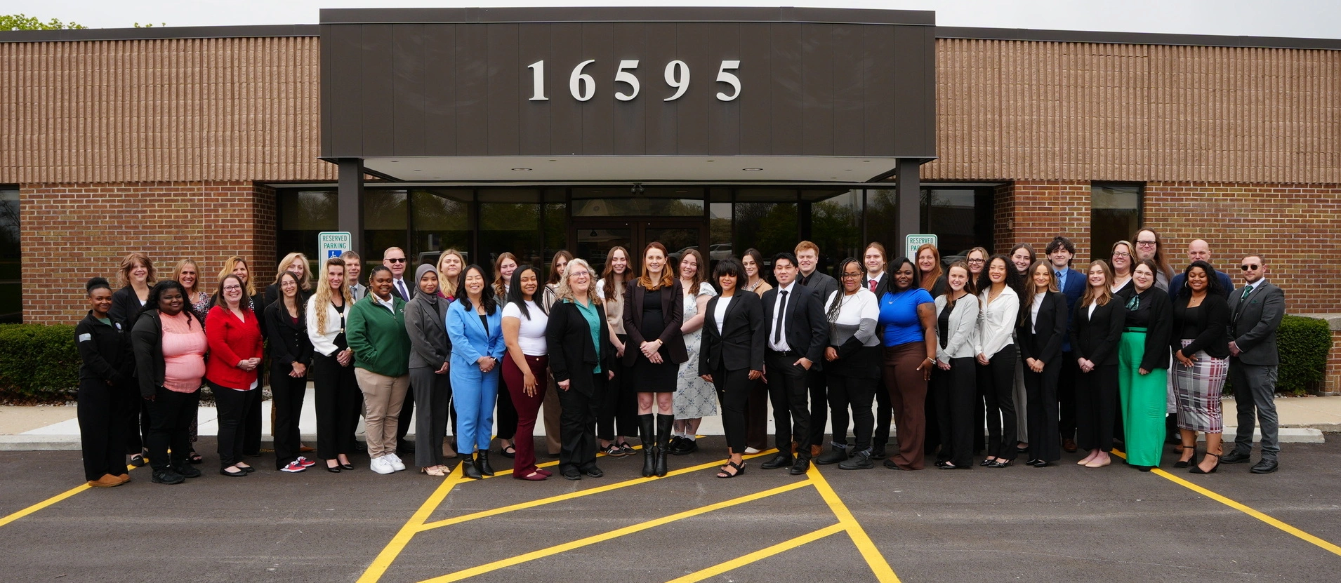 Group of diverse professionals standing outside a brick building with address number 16595 visible above the entrance.