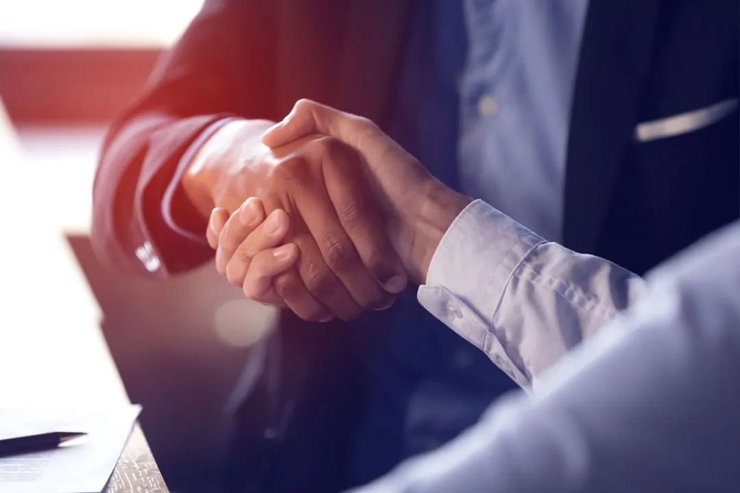 Two individuals in business attire shaking hands over a desk with documents.
