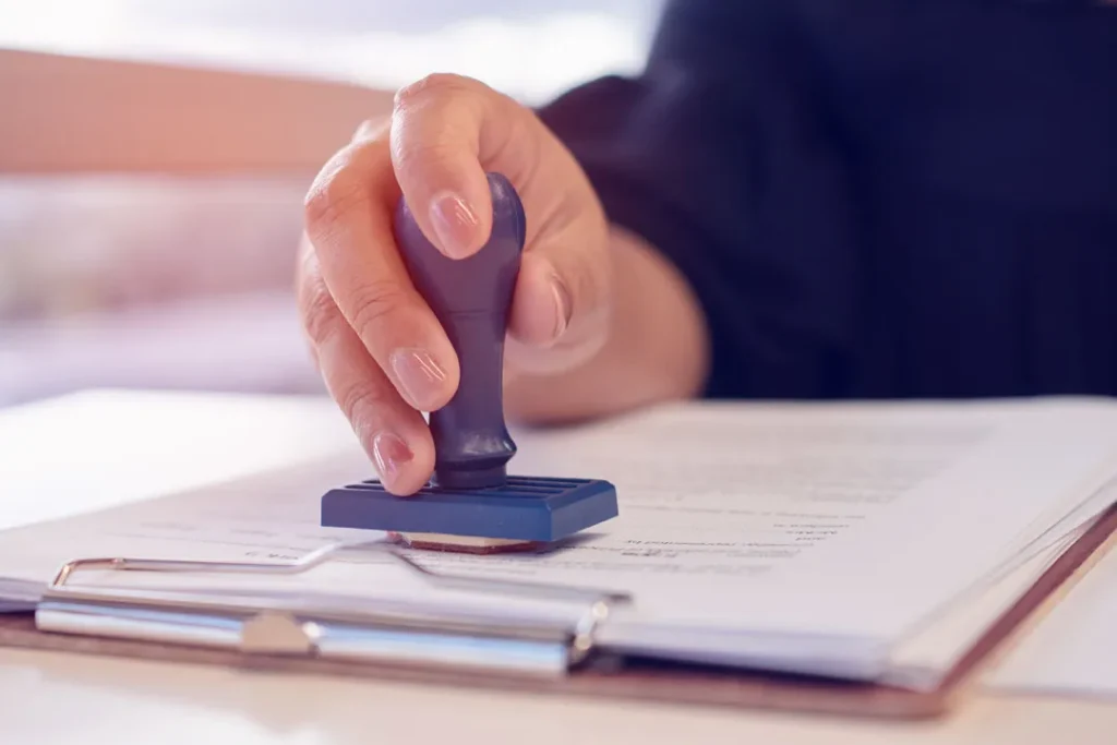 Close-up of hand using blue rubber stamp on document attached to clipboard.