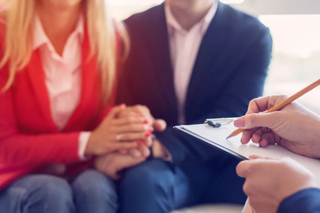 Couple holding hands during a consultation, with a professional taking notes on a clipboard.