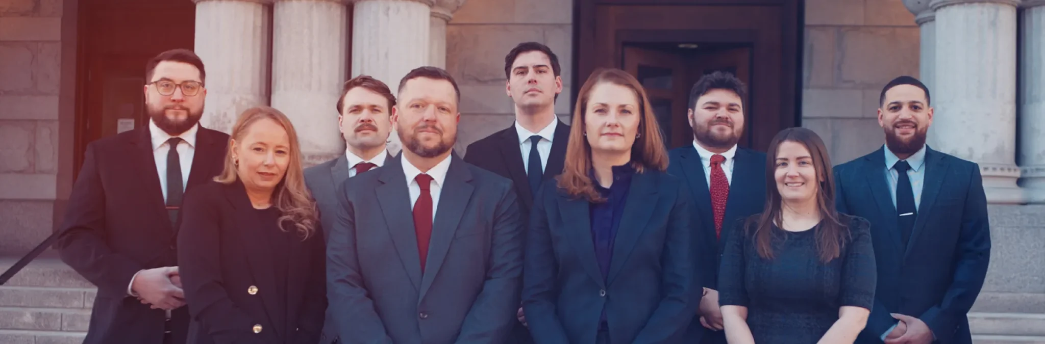 Group of nine professionally dressed men and women standing outside a stone building with columns.