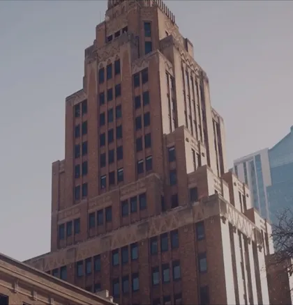 Alt text: Tall brown brick Art Deco skyscraper under clear sky with adjacent modern glass building.