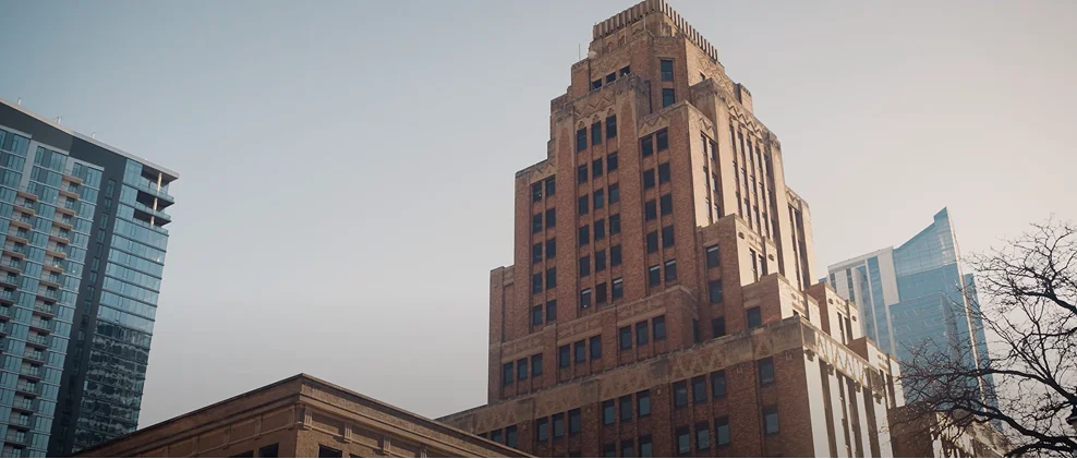 View of a tall, brown brick historic building with modern glass skyscrapers in the background under a clear sky.