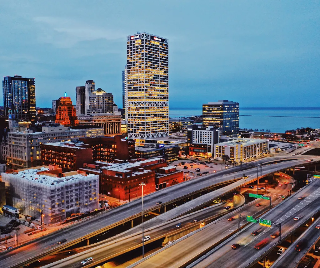 Aerial view of a city skyline at dusk with illuminated buildings and busy highways.