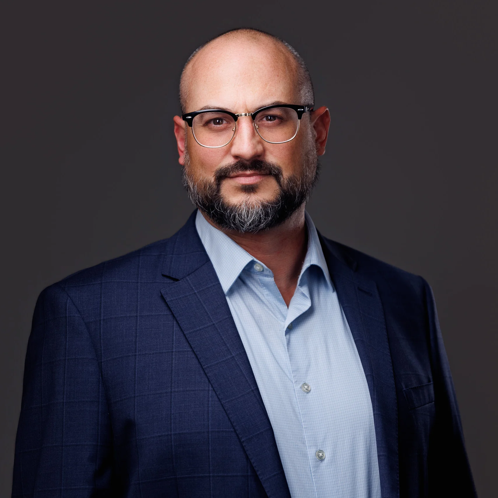 Professional portrait of a bald man with a beard, glasses, blue shirt, and navy blazer.