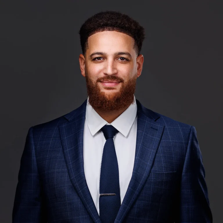 Professional portrait of a smiling man with a beard wearing a navy blue suit and tie.