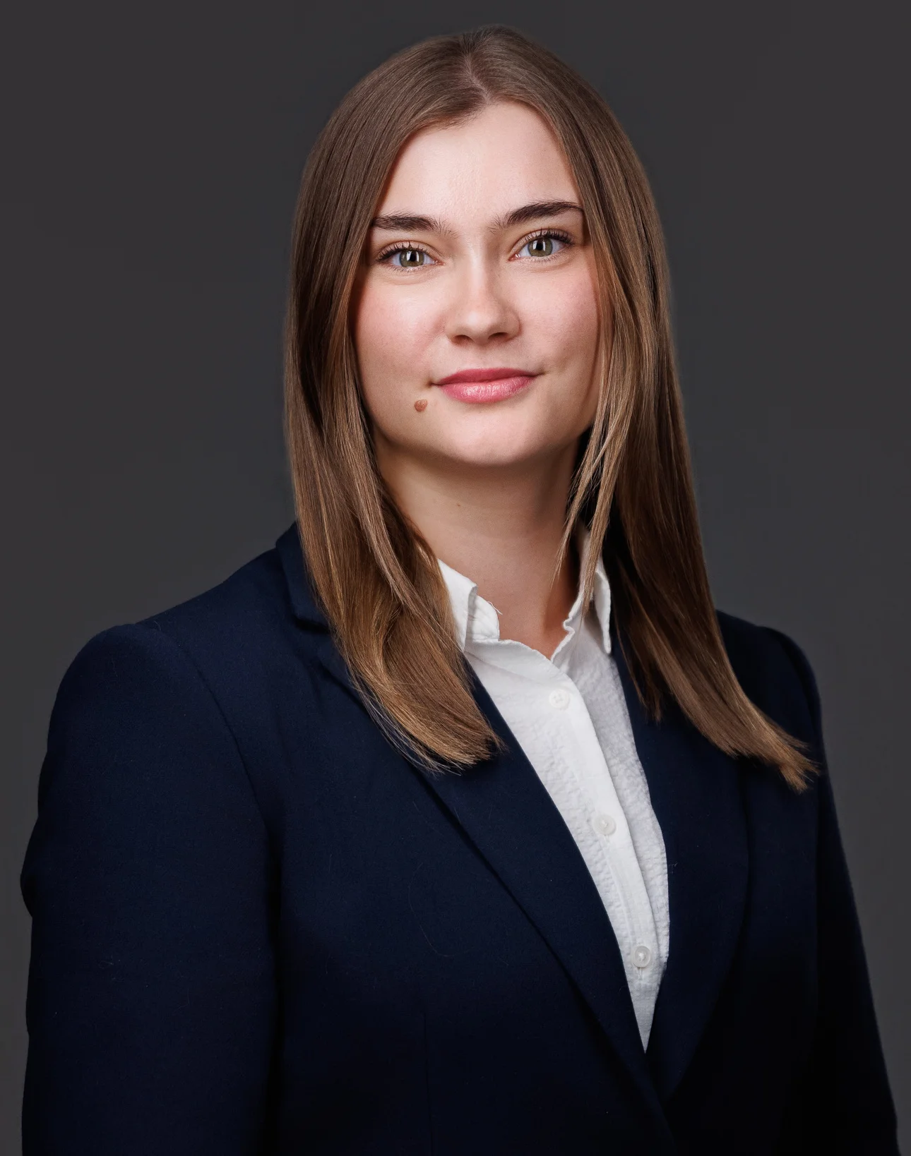 Professional headshot of a young woman with straight brown hair, wearing a navy blazer and white blouse.