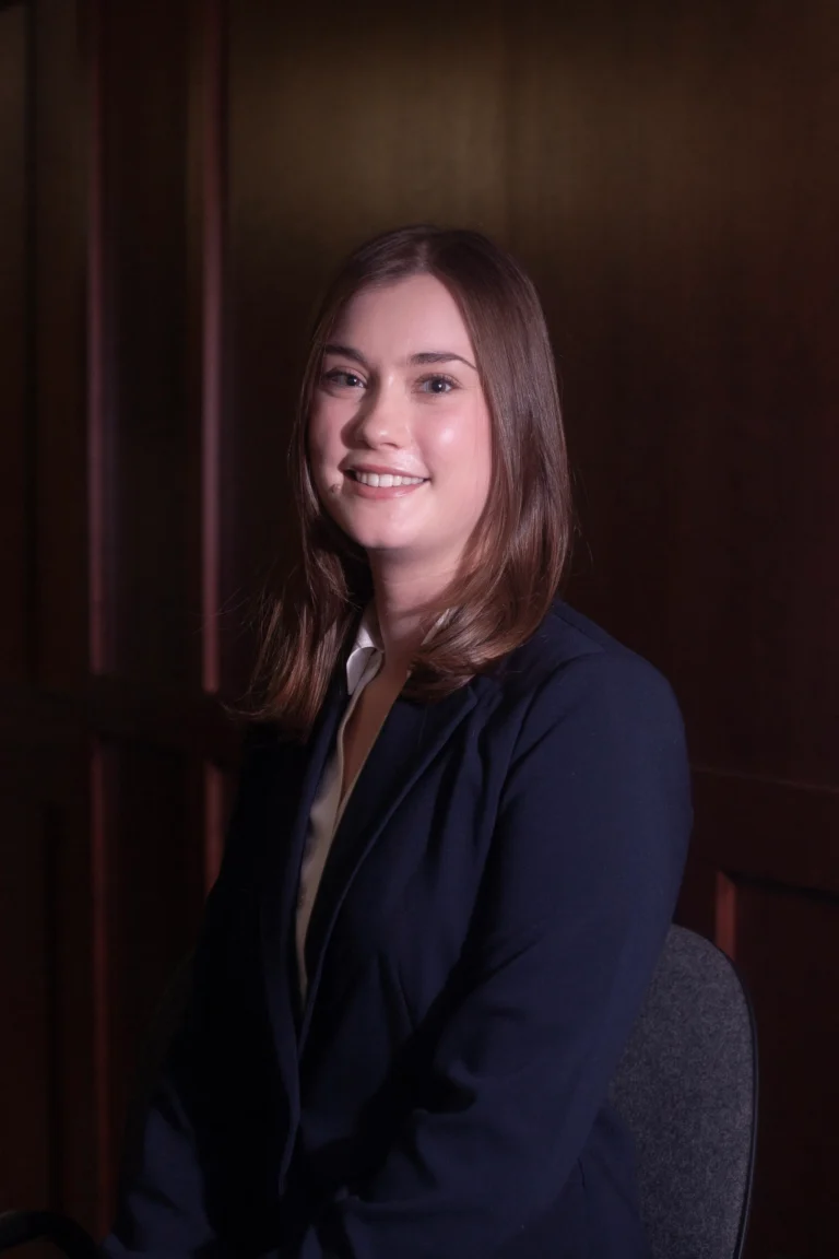 Professional portrait of a smiling young woman with brown hair wearing a dark blazer.