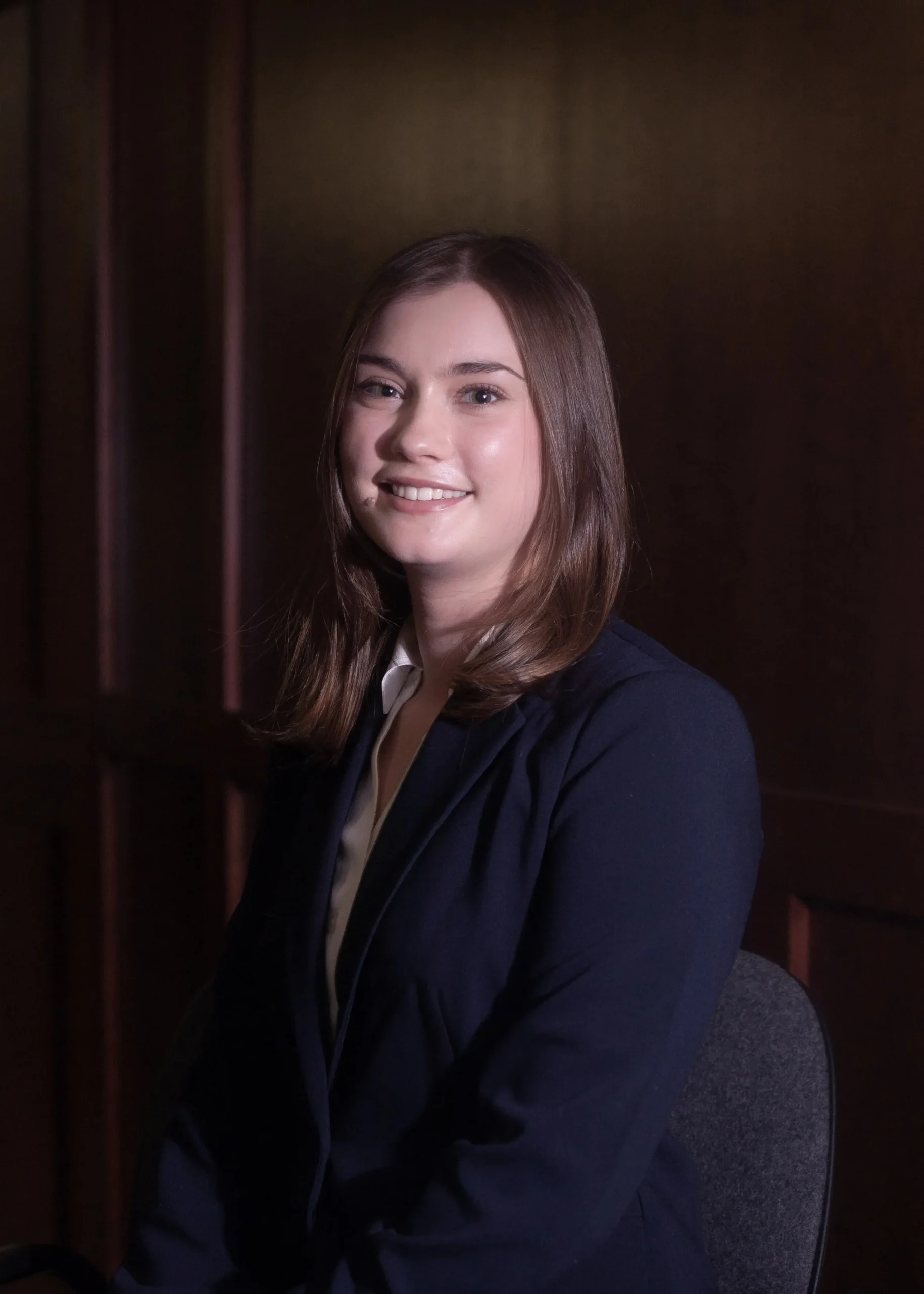 Portrait of a smiling woman with brown hair wearing a navy blazer and white blouse.