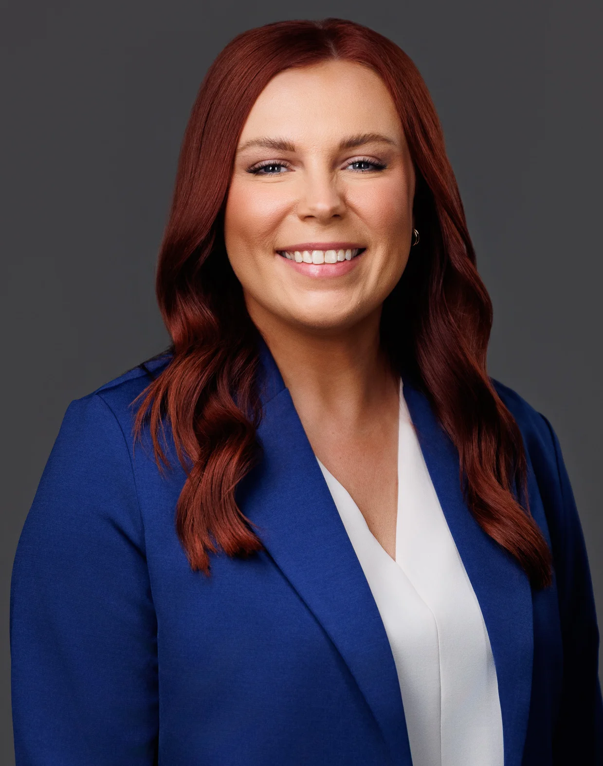 Professional headshot of a smiling woman with red hair, wearing a blue blazer and white blouse.