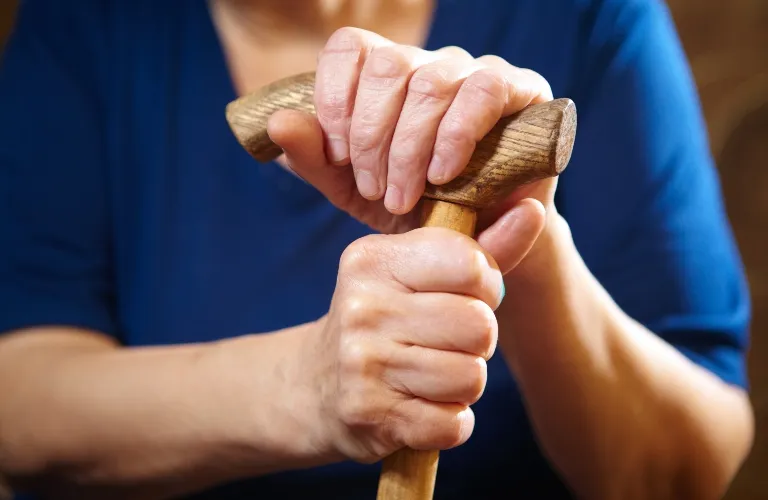 Close-up of elderly hands gripping a wooden cane, person wearing a blue shirt.