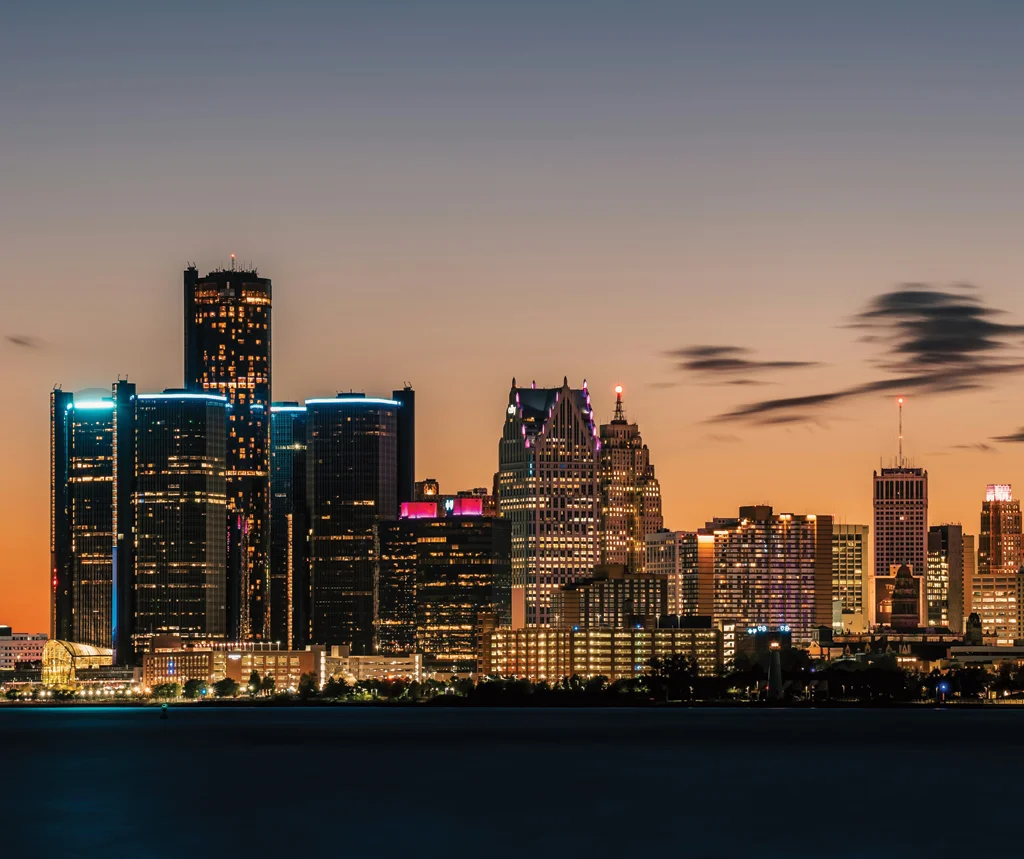 Panoramic view of a city skyline at dusk with illuminated skyscrapers and a colorful sunset sky.