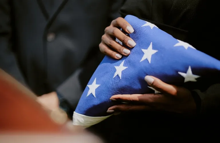 Hands holding a folded American flag with white stars on blue fabric, wearing black clothing.
