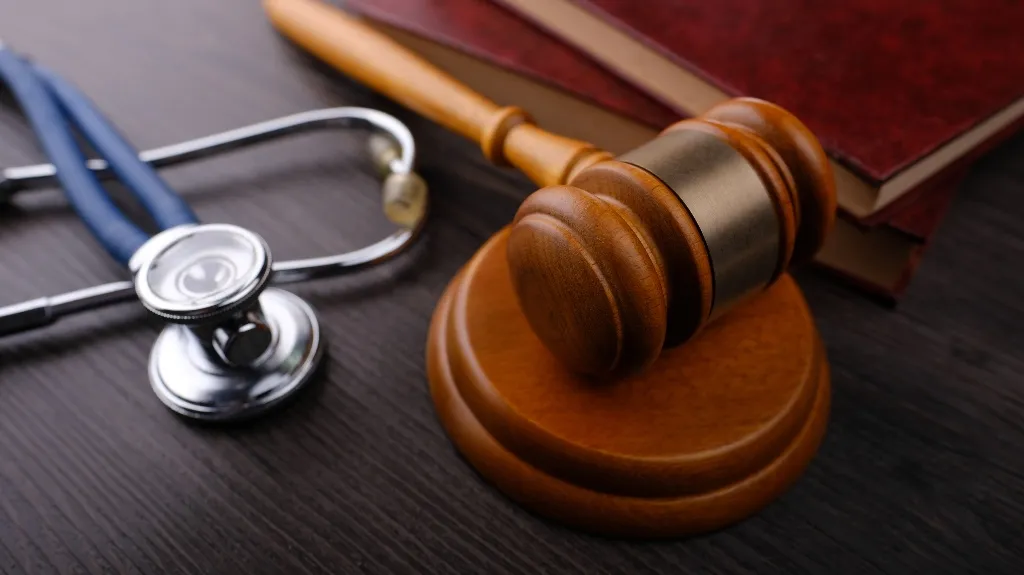Wooden judge's gavel, stethoscope, and stacked red legal books on dark wooden surface.
