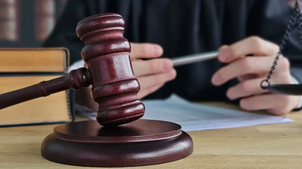 Close-up of a wooden judge's gavel on a desk with legal books and a person holding a pen.