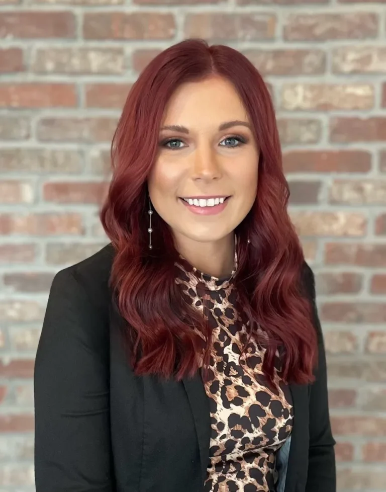 Professional portrait of a smiling woman with red hair, leopard print blouse, and black blazer.