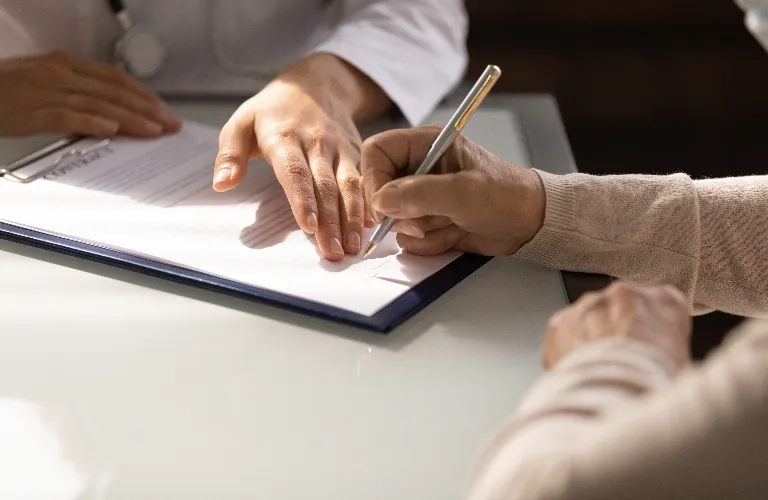 Two individuals, one in a white coat, the other signing a document on a clipboard.