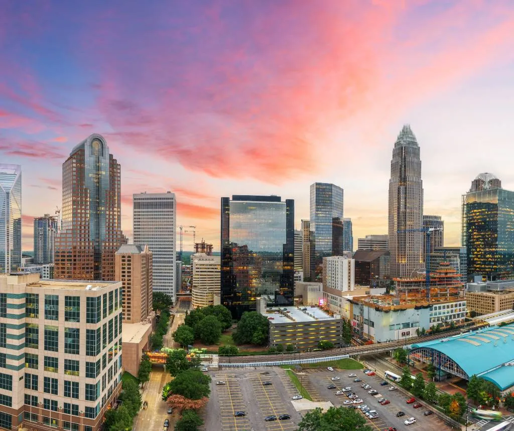 Aerial view of a modern city skyline with skyscrapers under a vibrant pink and purple sunset sky.