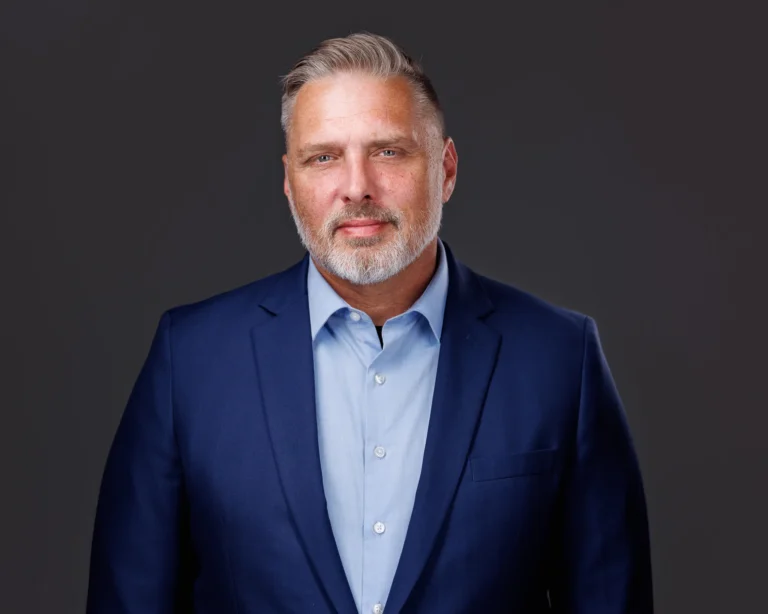 Portrait of a middle-aged man with gray hair and beard, wearing a blue suit and light blue shirt.