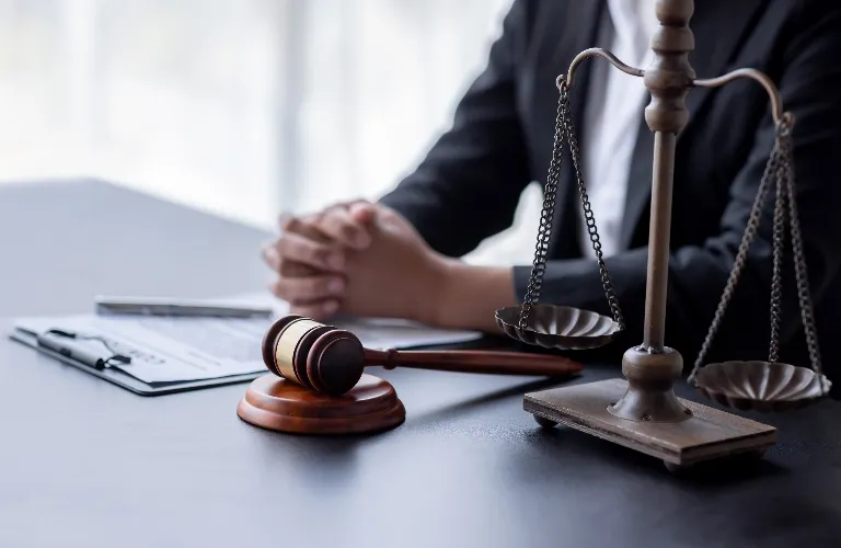 Close-up of a judge's gavel, scales of justice, and a person in a suit with clasped hands.
