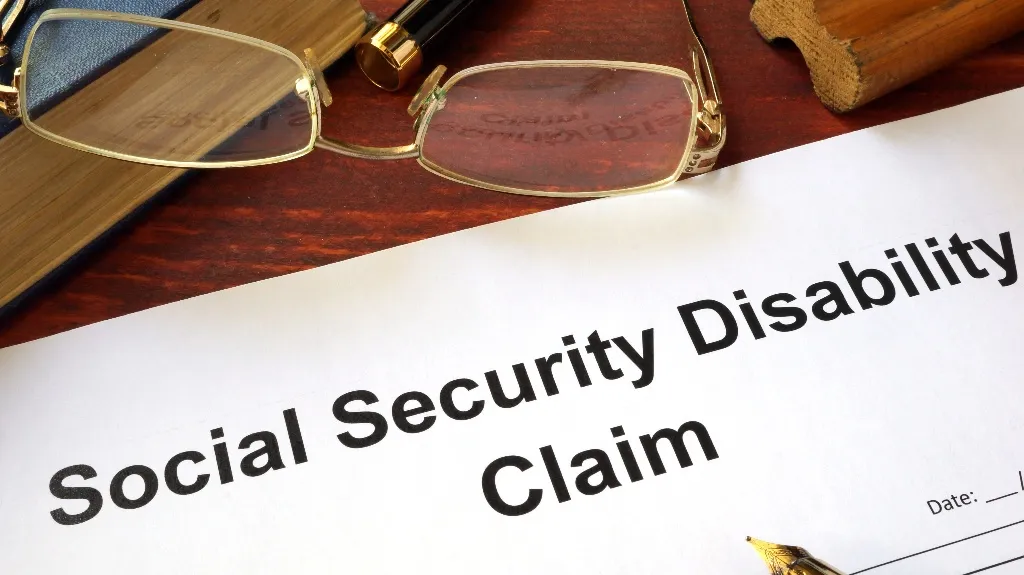 Close-up of a Social Security Disability Claim form on a wooden desk with gold-rimmed glasses and a fountain pen.