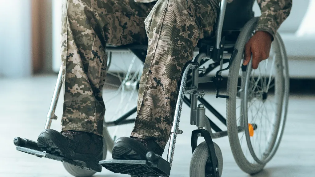 Close-up of a person in camouflage military uniform seated in a wheelchair indoors.