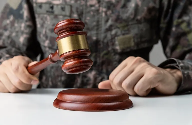 Person in military uniform holding a wooden judge's gavel above a sound block.