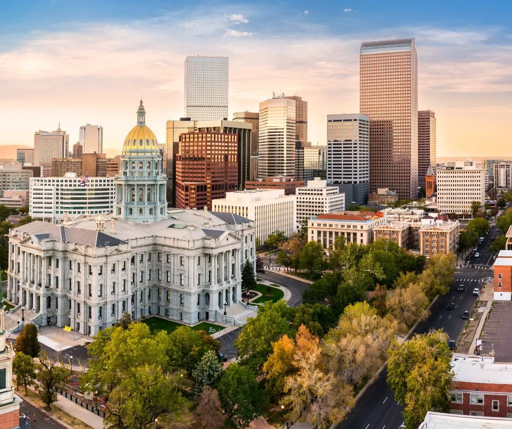 Aerial view of Denver cityscape at sunset with Colorado State Capitol and surrounding skyscrapers.