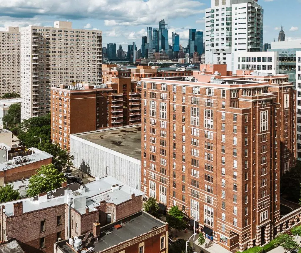 Aerial view of urban residential buildings with a distant city skyline under a partly cloudy sky.