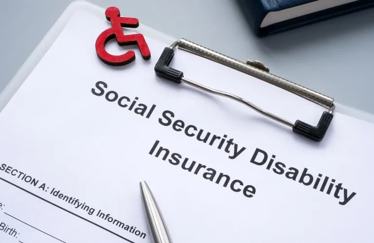 Clipboard with Social Security Disability Insurance form, red disability symbol, and pen.