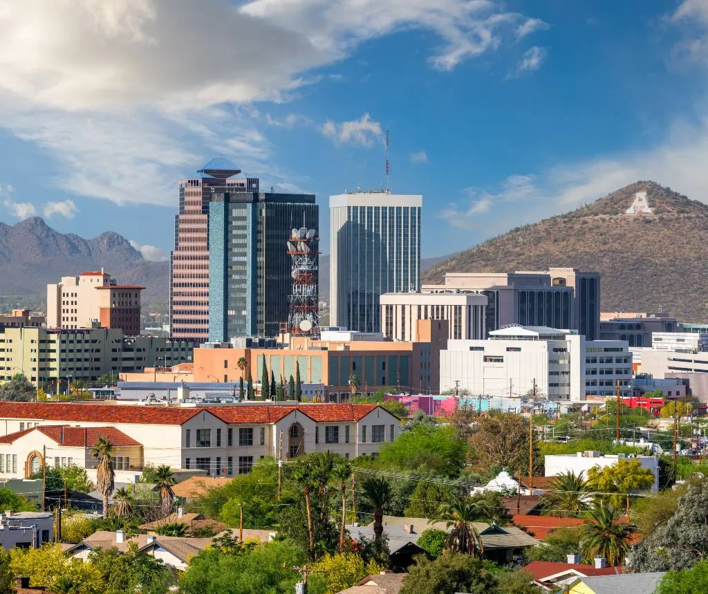 Cityscape of Tucson, Arizona with modern buildings, greenery, and a mountain featuring a large white "A" on its slope.