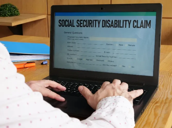 Person typing on a laptop displaying a Social Security Disability Claim form on screen.