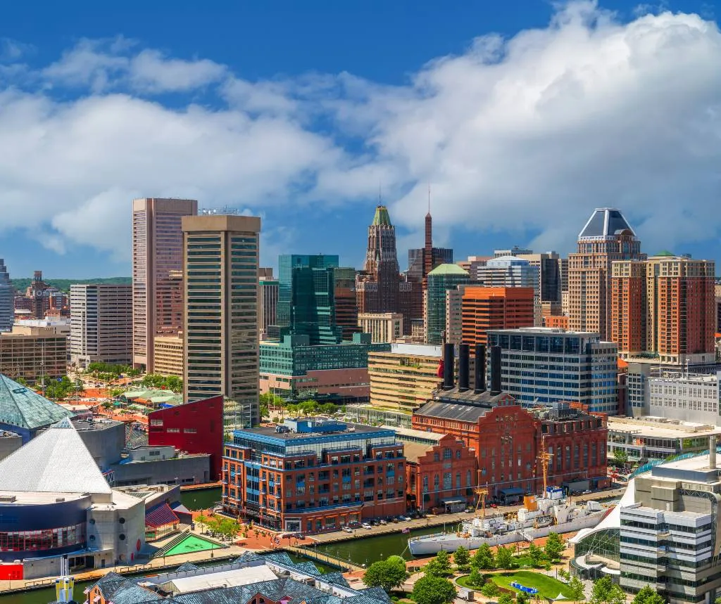 A vibrant city skyline featuring diverse modern and historic buildings under a partly cloudy blue sky.
