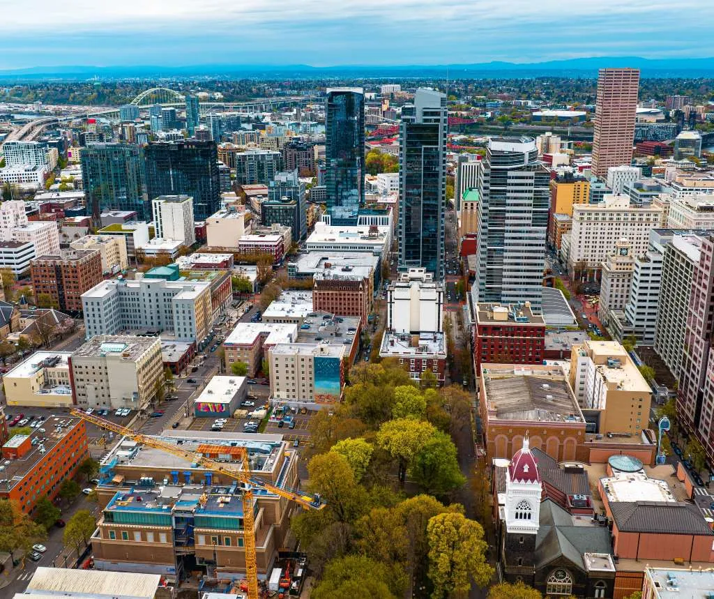 Aerial view of a cityscape with skyscrapers, mid-rise buildings, green trees, and construction cranes.