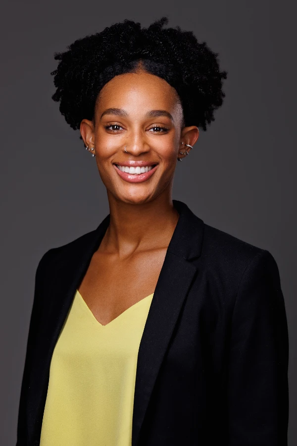 Professional portrait of a smiling woman with natural curly hair, wearing a yellow blouse and black blazer.