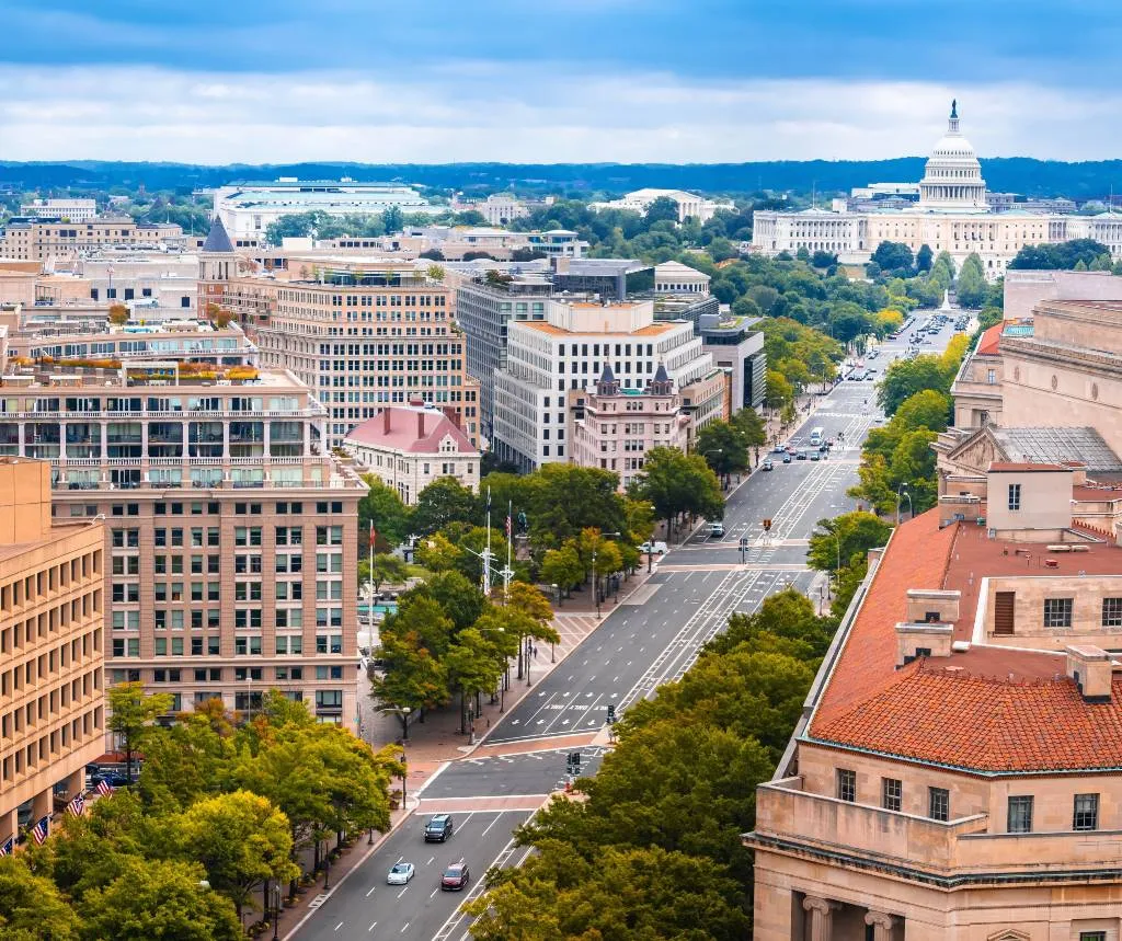 Aerial view of a city street lined with trees and buildings, leading to the U.S. Capitol.