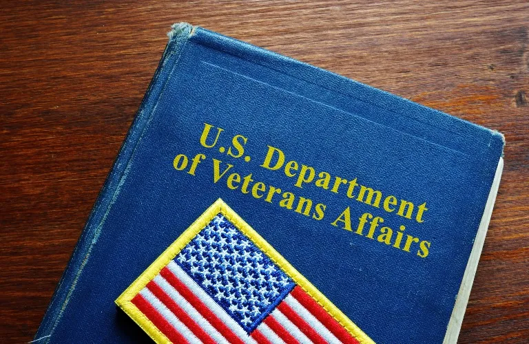 Blue booklet with U.S. Department of Veterans Affairs gold text and an embroidered American flag patch.