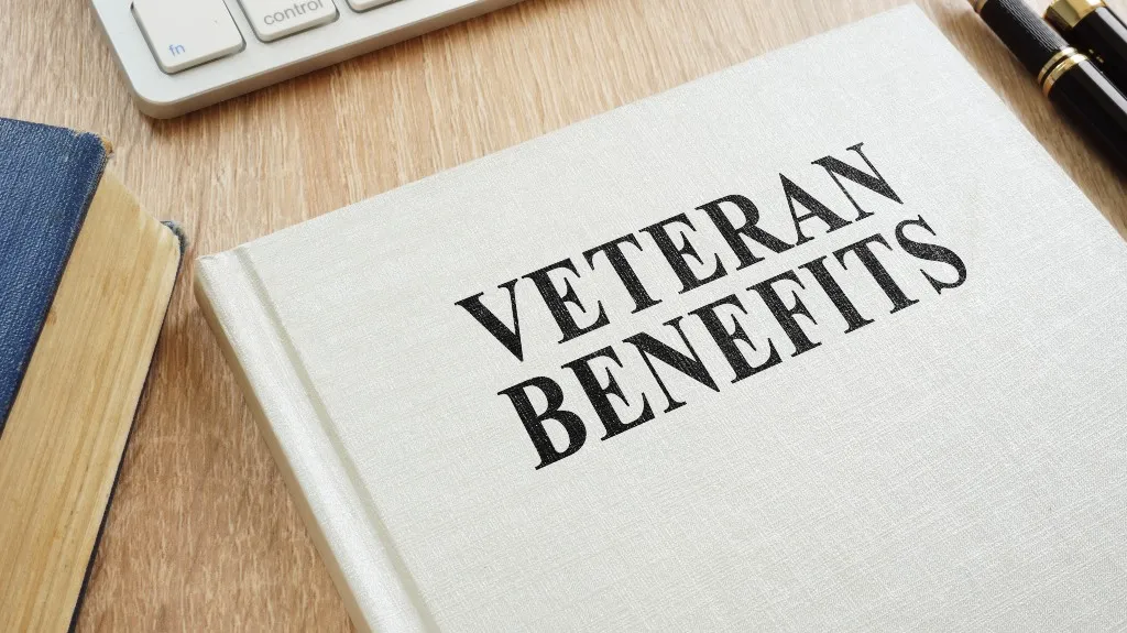 Close-up of a white book titled "VETERAN BENEFITS" on a wooden desk.