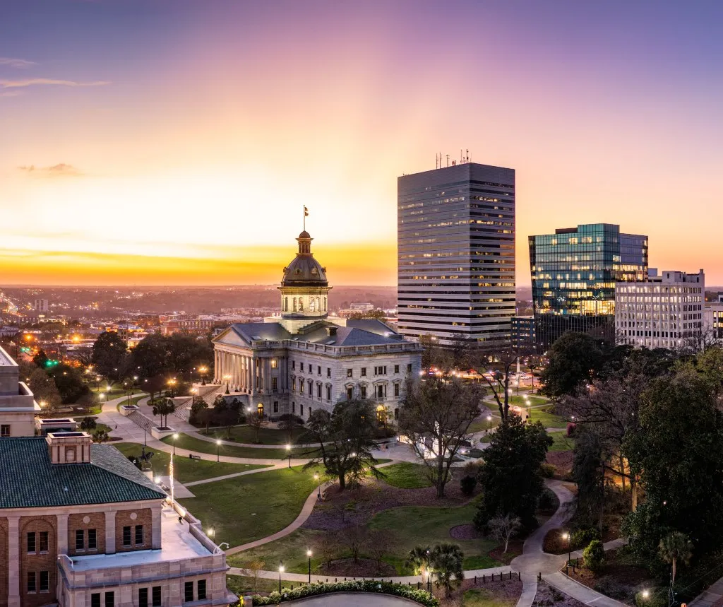 Aerial view of a historic building with a dome, modern skyscrapers, and a sunset sky.
