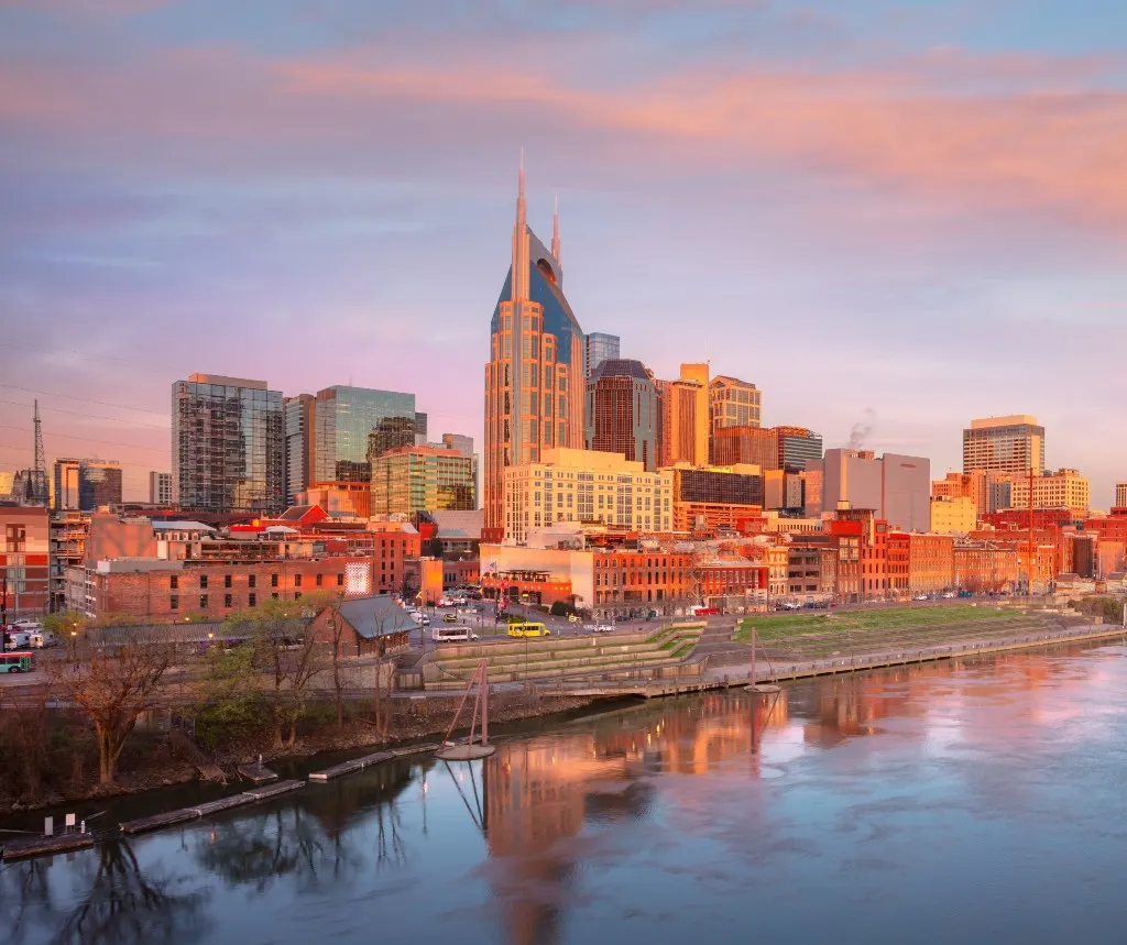 Panoramic view of a city skyline at sunset with reflective river and modern buildings.