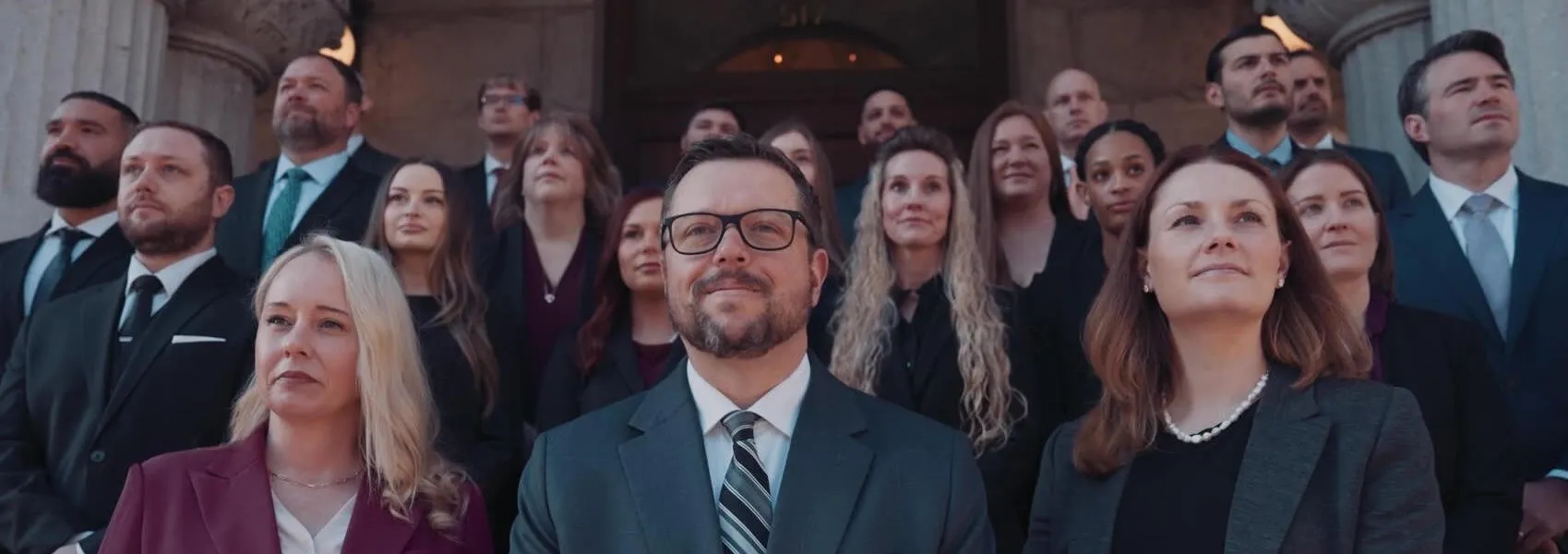 Group of professionally dressed men and women standing on stone steps outside a formal building.